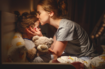 mother puts her daughter to bed and kisses her in   evening - Powered by Adobe