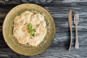 top view of gourmet italian ravioli with ricotta on plate and fork with knife on wooden table