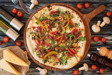 top view of baked delicious pizza with vegetables, cheese and meat on wooden chopping board