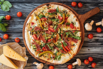 top view of delicious pizza with vegetables and meat on wooden chopping board