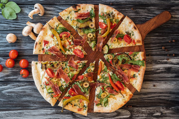 top view of sliced delicious pizza with vegetables and meat on wooden cutting board - Powered by Adobe