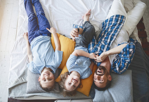 Top view portrait of happy boys lying on cozy bed near satisfied daddy. Glad dad resting with happy children concept
