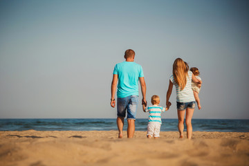 Young happy loving family with small kids walking at beach together near the ocean, happy lifestyle family concept. Back view