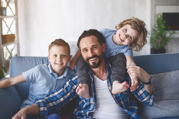 Portrait of positive father and cheerful sons looking at camera. Glad parent and children concept