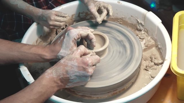 The potter teaches the child to work on a potter's wheel. adults and children's hands close-up.