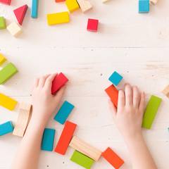 hand of a child playing with colorful wooden toy blocks and building shapes.