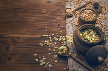 Malt and hop in wooden pots on burlap cloth on brown wooden table background with copy space.