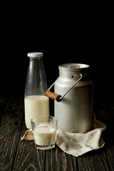 milk in bottle, glass and aluminium can on sackcloth on black background