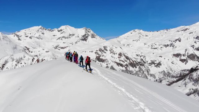 Aerial video. Group of ski touring on skin uphill in a line. Drone shot Ski touring in big mountains, beautiful landscape with high peaks in background. Winter adventure and breath taking view
