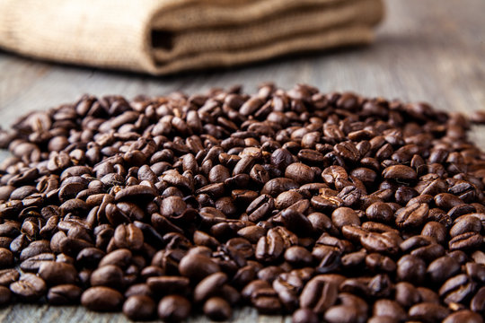 Pile of roasted coffee beans on a wooden table with hessain sack in background