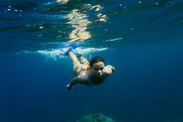 Fototapeta na wymiar underwater photo of young woman in swimming suit diving in ocean alone