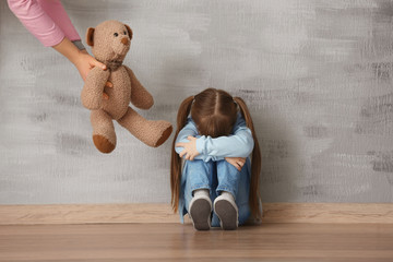 Female psychologist giving teddy bear to sad little girl indoors