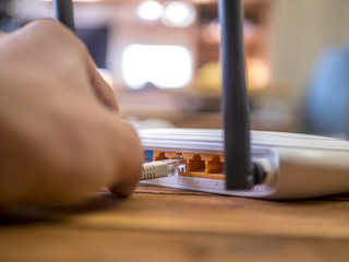 close up hand inserting ethernet wire in wi-fi router on wooden table