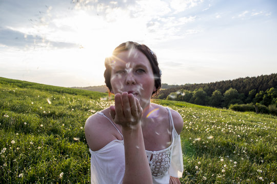 Young woman blows dandelion flower