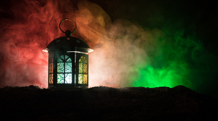 Fototapeta na wymiar Ornamental Arabic lantern with burning candle glowing at night on dark toned foggy background. Festive greeting card, invitation for Muslim holy month Ramadan Kareem.
