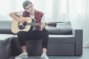 pensive teenager playing acoustic guitar at home