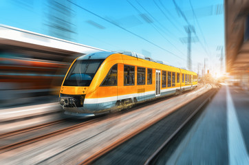 High speed orange train in motion on the railway station at bright day. Modern intercity train with...