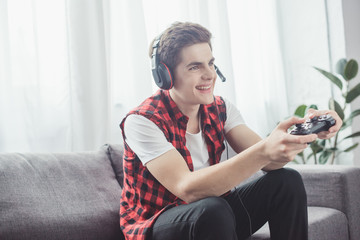happy teenager with headset playing video game with joystick at home