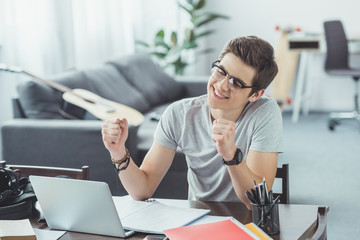 excited student with laptop doing homework at home