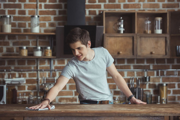 handsome teenager cleaning table with rag in kitchen