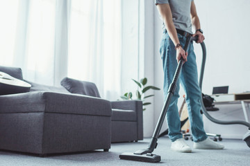 cropped view of young man cleaning floor with vacuum cleaner