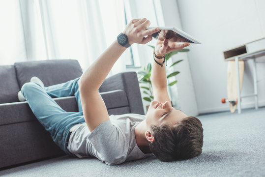 handsome teen boy using digital tablet while lying on floor