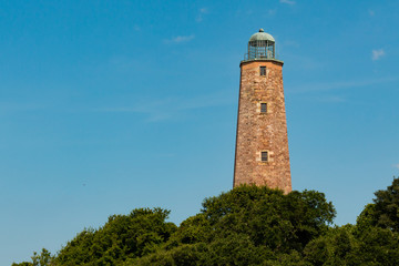 The Old Cape Henry Lighthouse, towers over nearby trees on a sunny summer day on the Fort Story military base.
