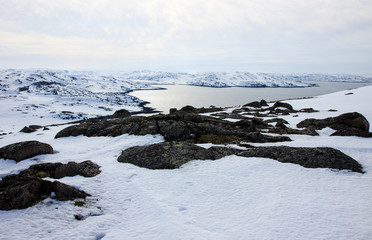 Russian Arctic View, North. Sky with clouds and blue sky reflection in water with waves and snow mountains background with stones grass foreground. Picturesque landscape view, nature scenery beauty