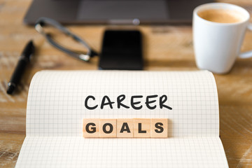 Closeup on notebook over wood table background, focus on wooden blocks with letters making Career Goals text