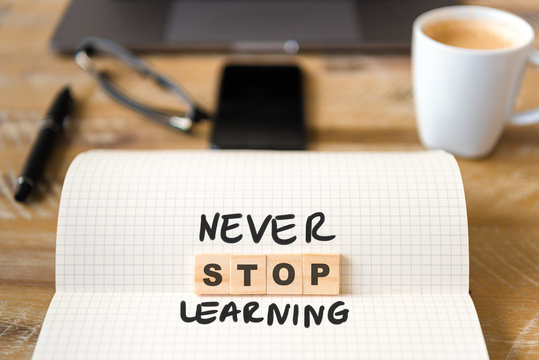 Closeup on notebook over wood table background, focus on wooden blocks with letters making Never Stop Learning text