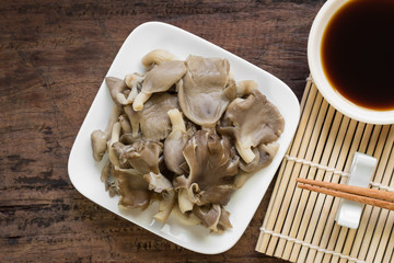 close up of steamed phoenix mushroom in a ceramic plate served with soy sauce on old wooden table. healthy food concept.