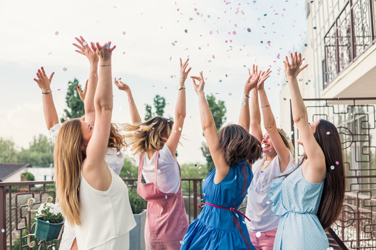 Girls Party. Beautiful Women Friends on the balcony Having Fun At Bachelorette Party. They are dancing in confetti with hands up