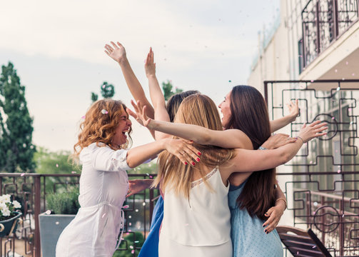 Girls Party. Beautiful Women Friends on the balcony Having Fun At Bachelorette Party. They are hugging in confetti with hands up