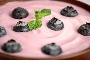 close up pink creamy homemade blueberries fruit yogurt with fresh green mint leaf on wooden table background