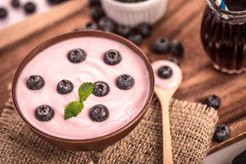 Obraz na płótnie Canvas close up pink creamy homemade blueberries fruit yogurt with the fresh green mint leaf on wooden table background ,top view or overhead shot