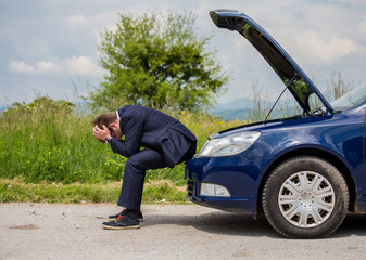 A broken car on the road, the driver is holding his head, an open hood, a car in failure
