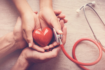 child and adult holding red heart with stethoscope, heart health,  health insurance concept