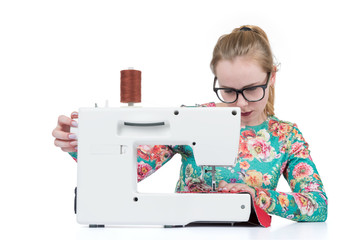 Young girl with glasses sews on a sewing machine, isolated on white background