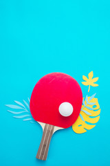 Ping pong beach set, flip flops, sunglasses and tropical leaves. Summer sports and recreation flat lay on a bright blue background with copy space.