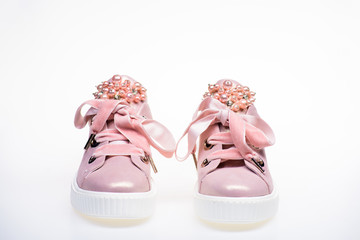 Glamorous sneakers concept. Cute shoes isolated on white background. Footwear for girls and women decorated with pearl beads. Pair of pale pink female sneakers with velvet ribbons.