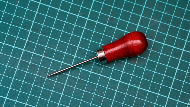 Tool of a tanner close-up. Awl lies on rug for cutting.