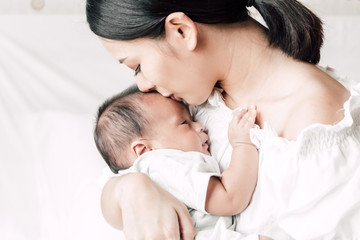 Mother holding baby in her arms and kiss in a white bedroom.Love of family concept