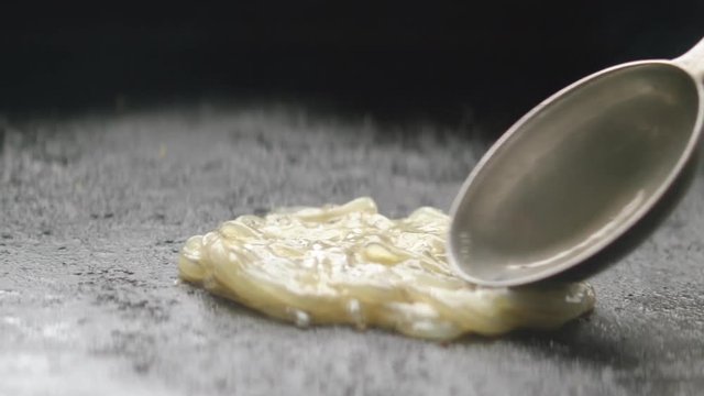 Close up of raw whitebait slowly poured and spread onto hot plate for cooking