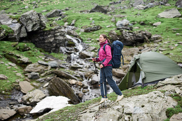 Cheerful young woman hiker smiling walking in the mountains valley with trekking poles tent on the background copyspace recreation lifestyle people harmony activity sports tourism exploring.