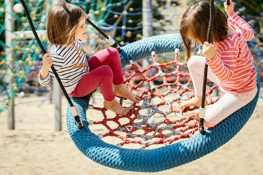 two little girls are swinging on a swing at the playground on a summer day
