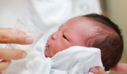 Newborn Baby drinking milk from glass cup.