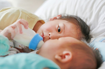 Close up Asian sister feeding milk from bottle for her brother and lying on the bed.