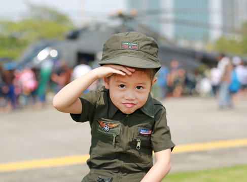 Portrait Of Asian Child Girl Wearing Airforce Pilot Suit Against Blur Helicopter Background.
