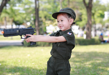 Little Asian child girl in pilot soldier suit costume with holding gun in hands at the garden.