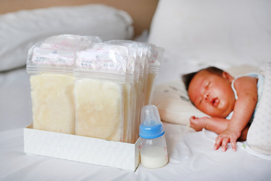 Frozen breast milk in plastic bag on the bed with infant baby sleeping.